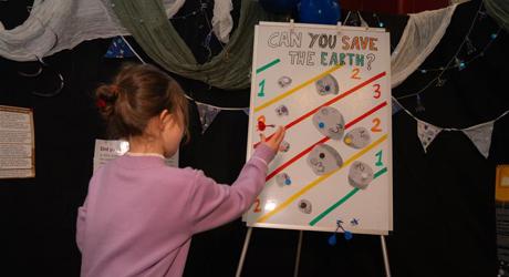 small female child throwing a dart at a board with can you save the earth written on it