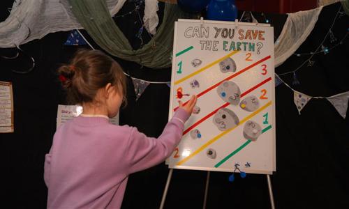 small female child throwing a dart at a board with can you save the earth written on it