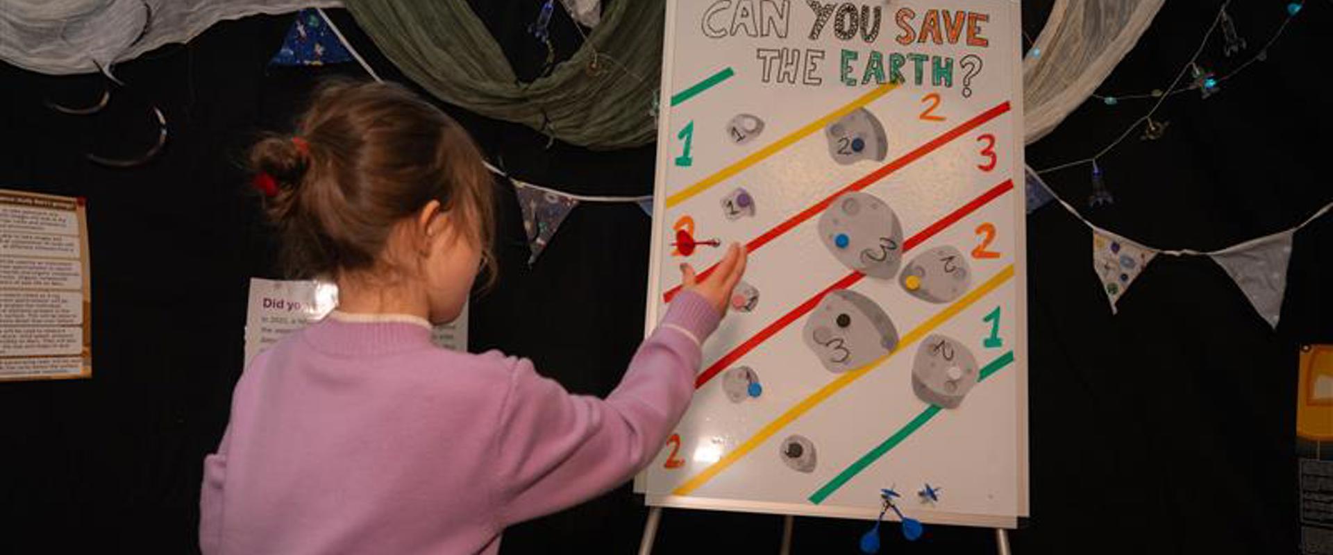 small female child throwing a dart at a board with can you save the earth written on it