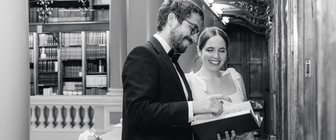 The bride and groom reading a book in the Upper Library (black and white image).