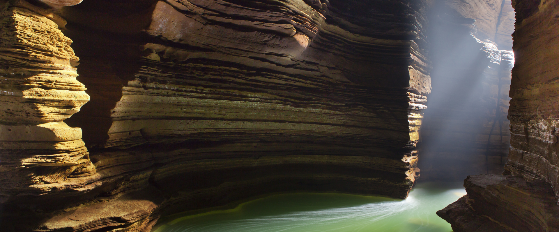 a green lake in a cavern with tall rock faces either side and the sun shining through the opening