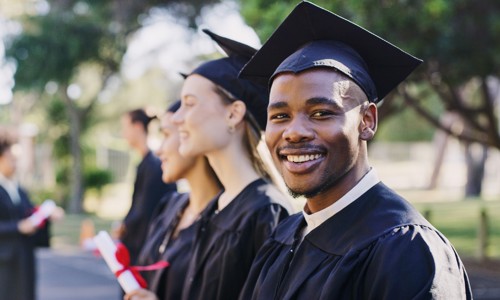 a black male student in graduation attire in foreground with female graduates next to him in the background