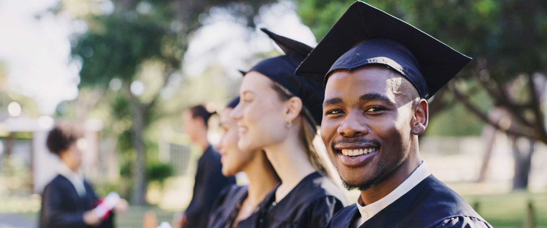 a black male student in graduation attire in foreground with female graduates next to him in the background