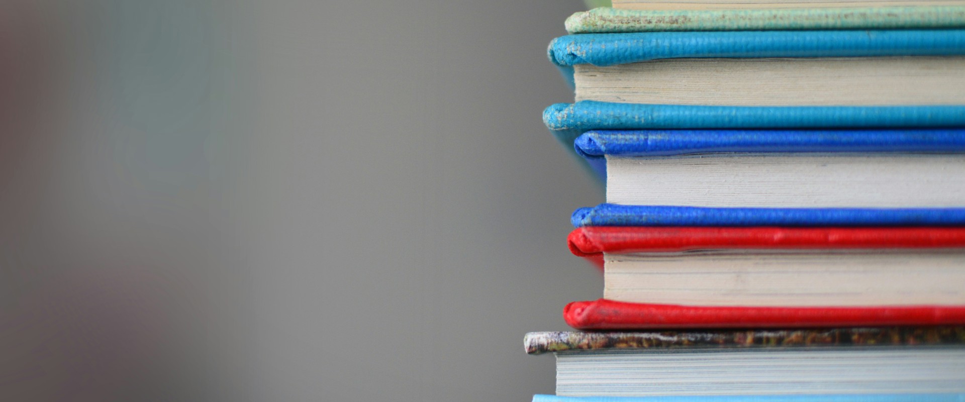 Six books piled one of top of the other, showing coloured edges of spines and covers against a grey background