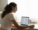 Woman on laptop with notepad studying