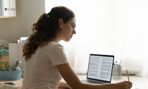 Woman on laptop with notepad studying