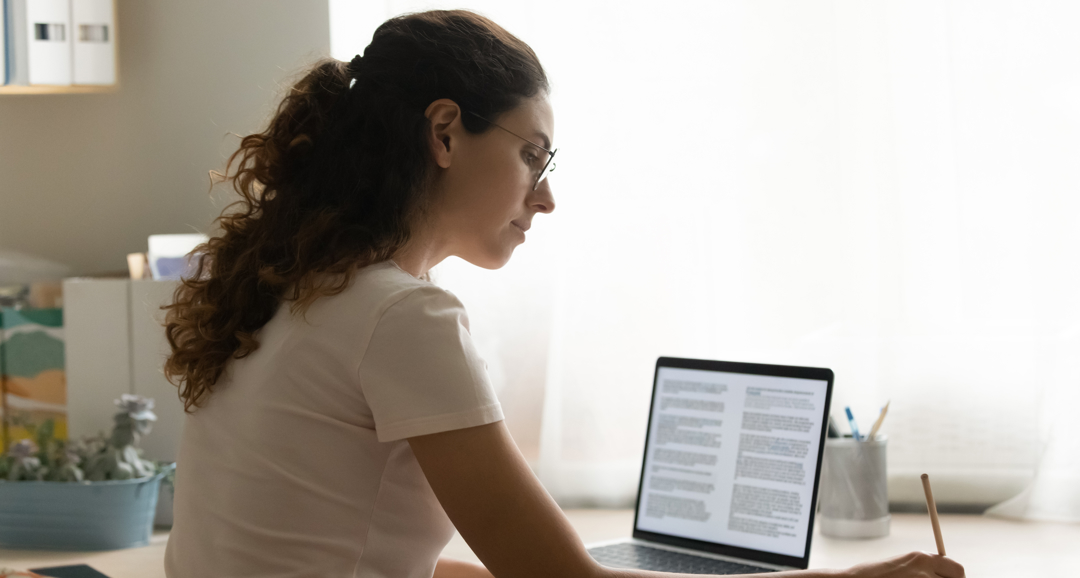 Woman on laptop with notepad studying