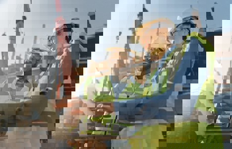 Two people in hardhats on site looking at a laptop