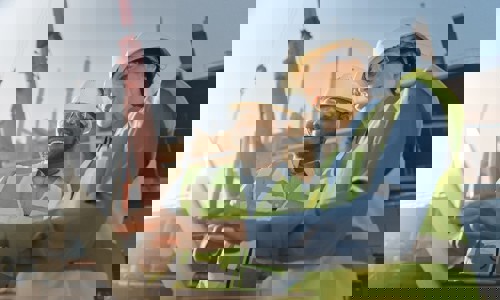 Two people in hardhats on site looking at a laptop