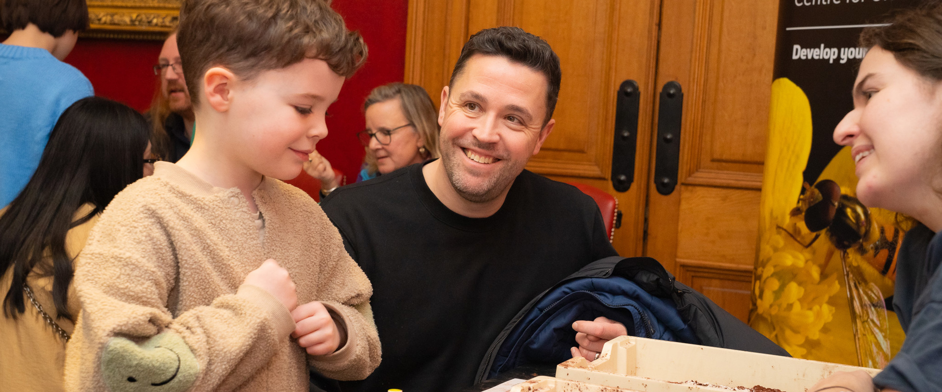 white man smiling at small white child who is looking at a box containing brown mud like substance