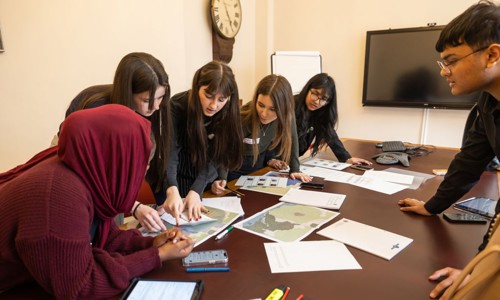 three white girls with two Asian girls and one Asian boy looking at maps on a table