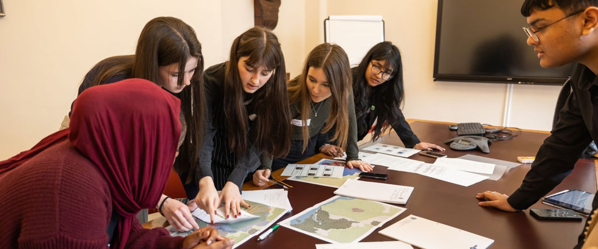 three white girls with two Asian girls and one Asian boy looking at maps on a table