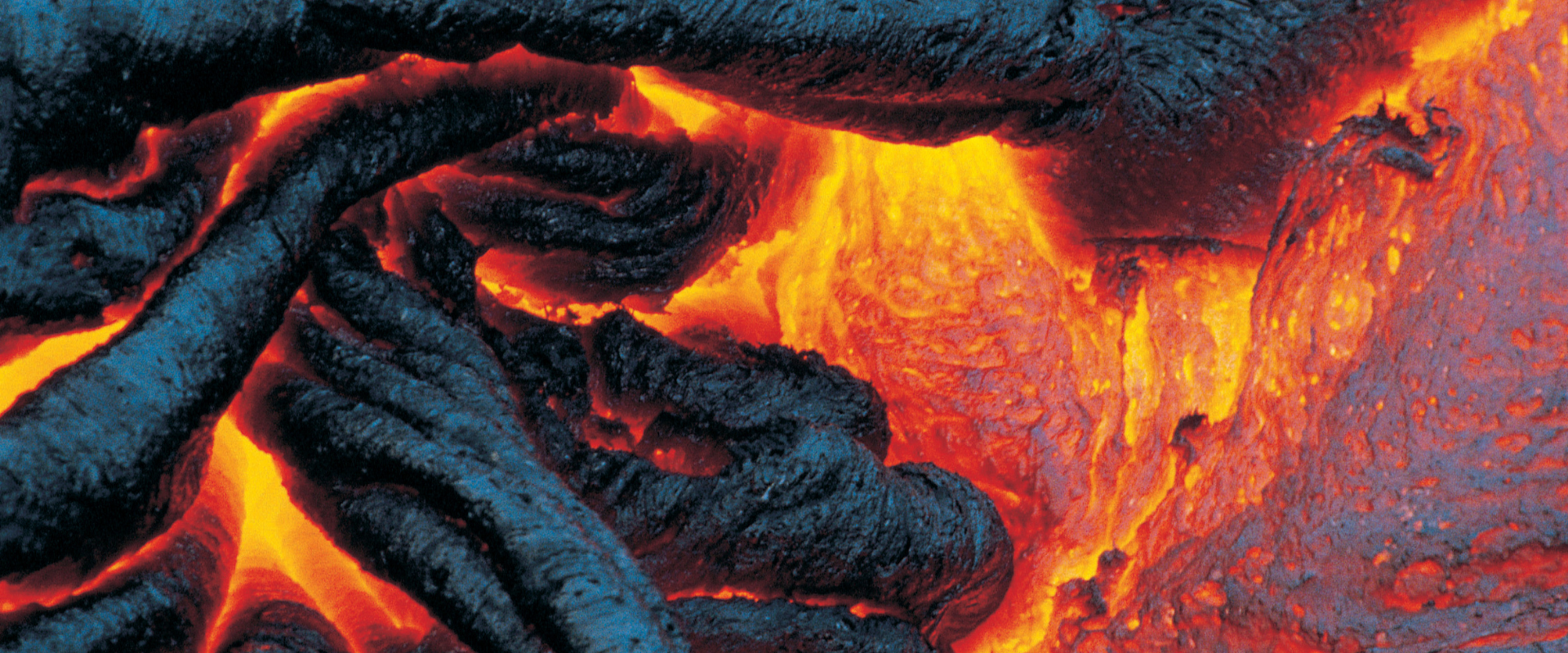 Close-up of flowing lava with bright, molten orange areas surrounded by dark, cooled lava formations.