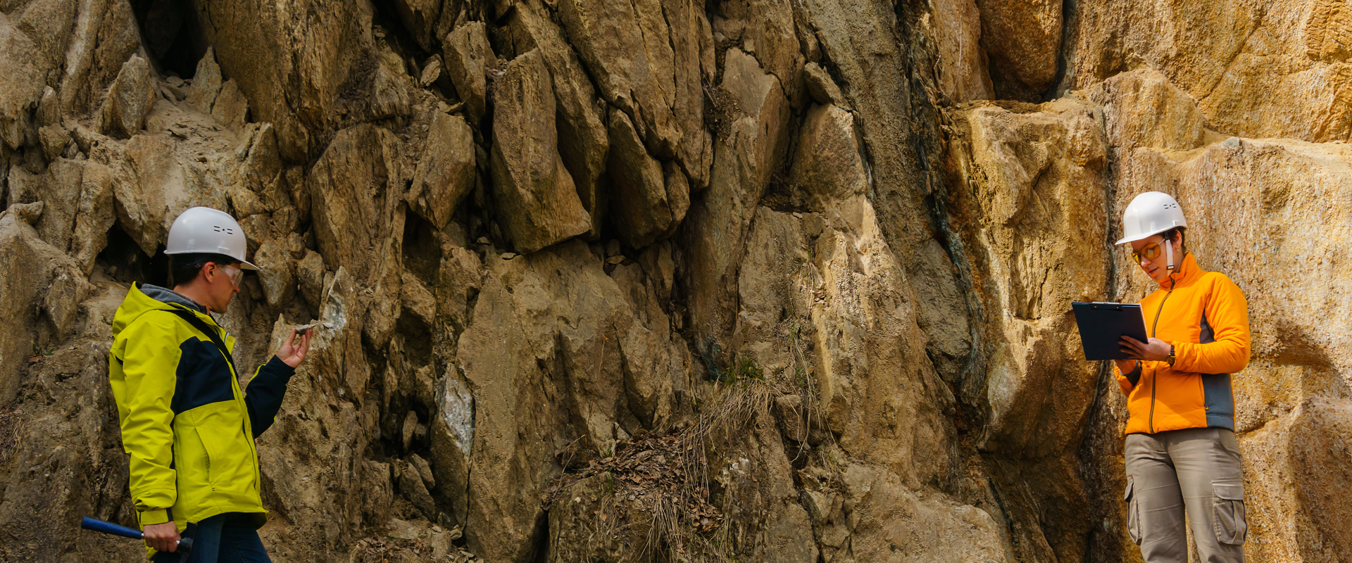 two people in high vis jackets and hard hats inspecting a rocky area