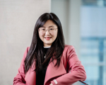 young east asian woman with long dark hair and glasses smiling wearing a pink jacket and dark blue jumper