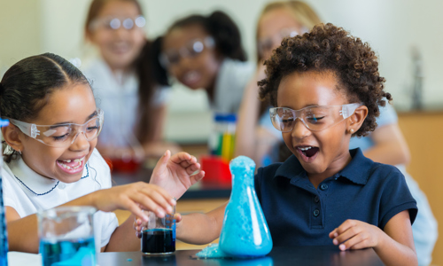 two small black girls smiling excitedly at their bubbling vial science experiment