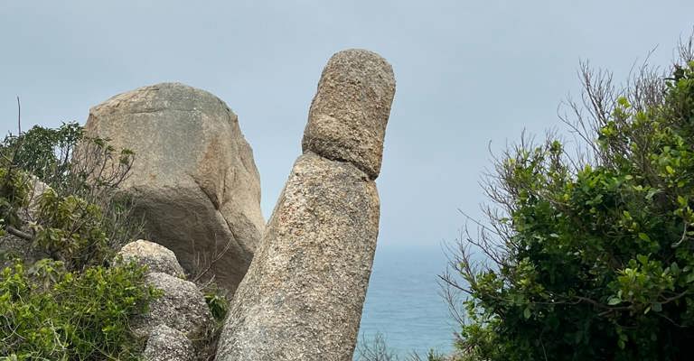 A tall rock with ocean in the background