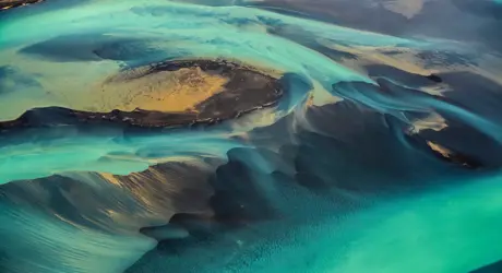 A unique green-coloured solar flare flowing through sandy dunes.