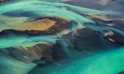 A unique green-coloured solar flare flowing through sandy dunes.