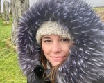 woman with a coat with a furry hood stood in front of tall stones