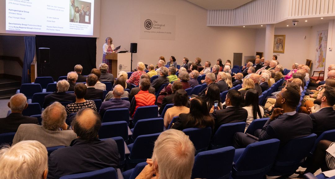 People seated in a lecture theatre listening to a woman speaking