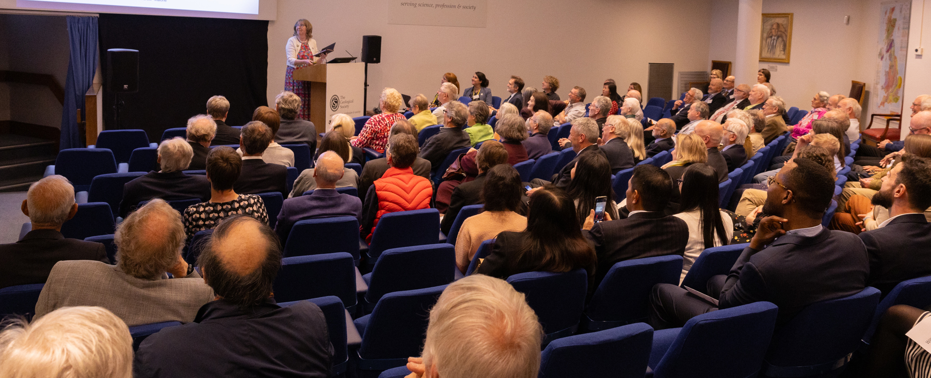 People seated in a lecture theatre listening to a woman speaking