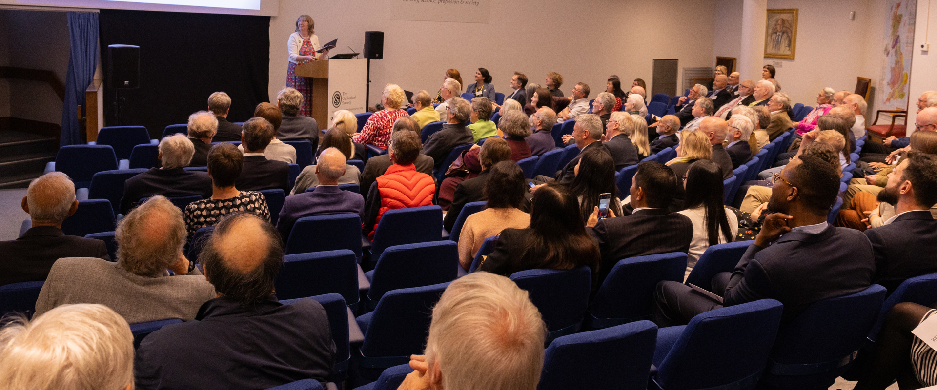 People seated in a lecture theatre listening to a woman speaking