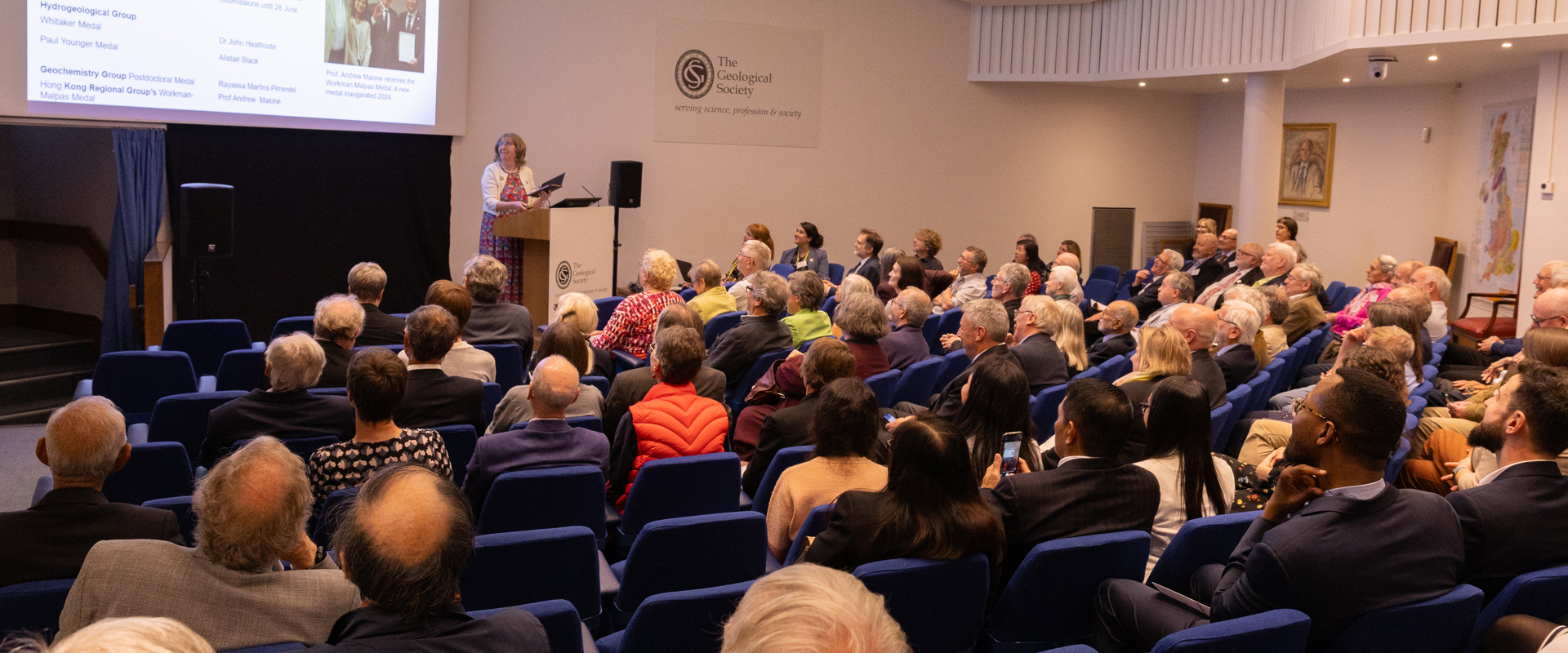 People seated in a lecture theatre listening to a woman speaking