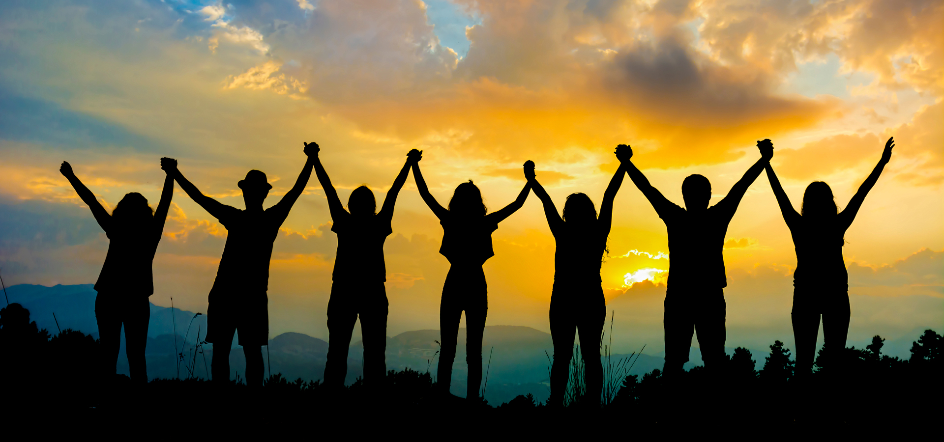 Silhouettes of a group of people holding hands with their arms in the air