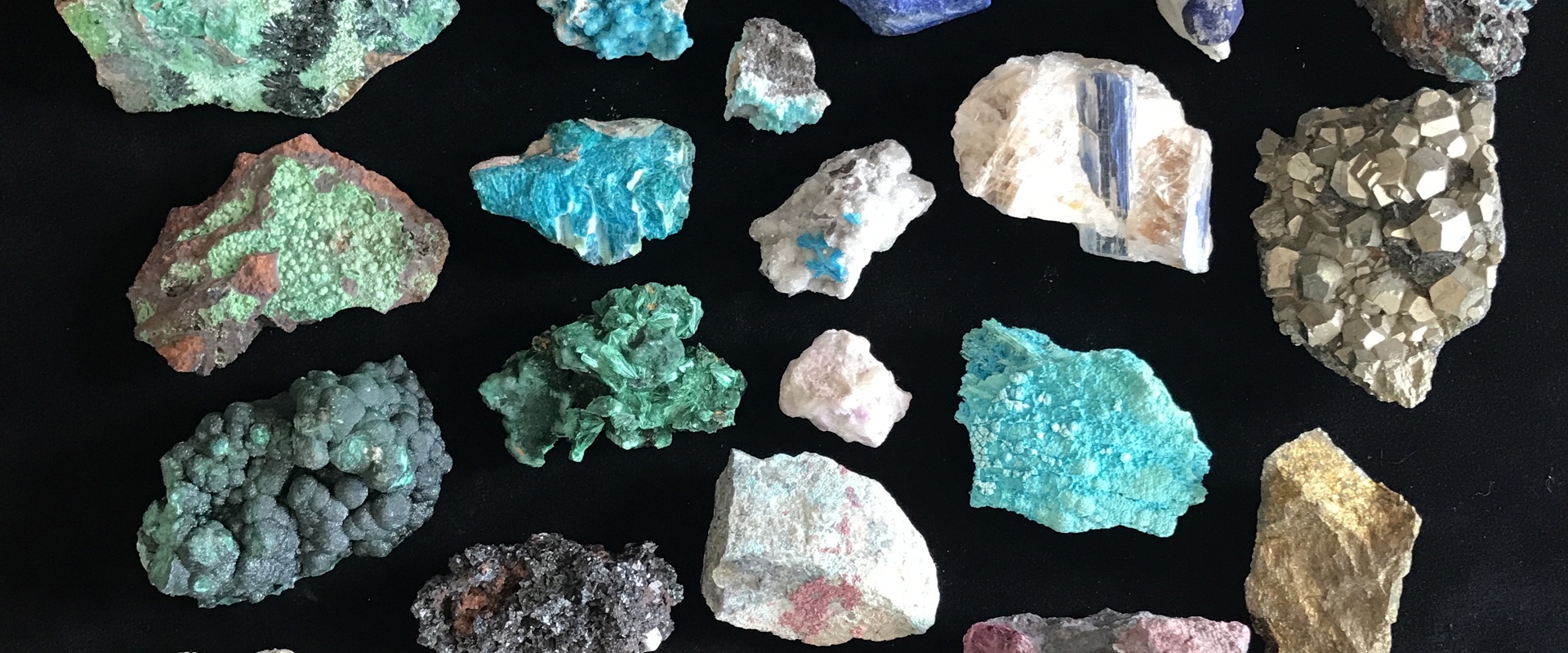 A collection of colourful mineral and rock specimens arranged in a grid on a black background. The assortment includes pieces in shades of turquoise, green, blue, purple, white, gold, and brown, with varied textures such as crystalline surfaces, rough edges, metallic clusters, and smooth formations.