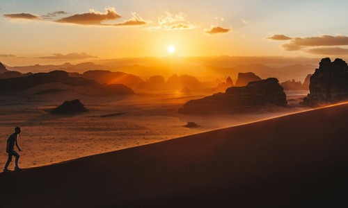 silhouette of man walking up a mountain with sun in background