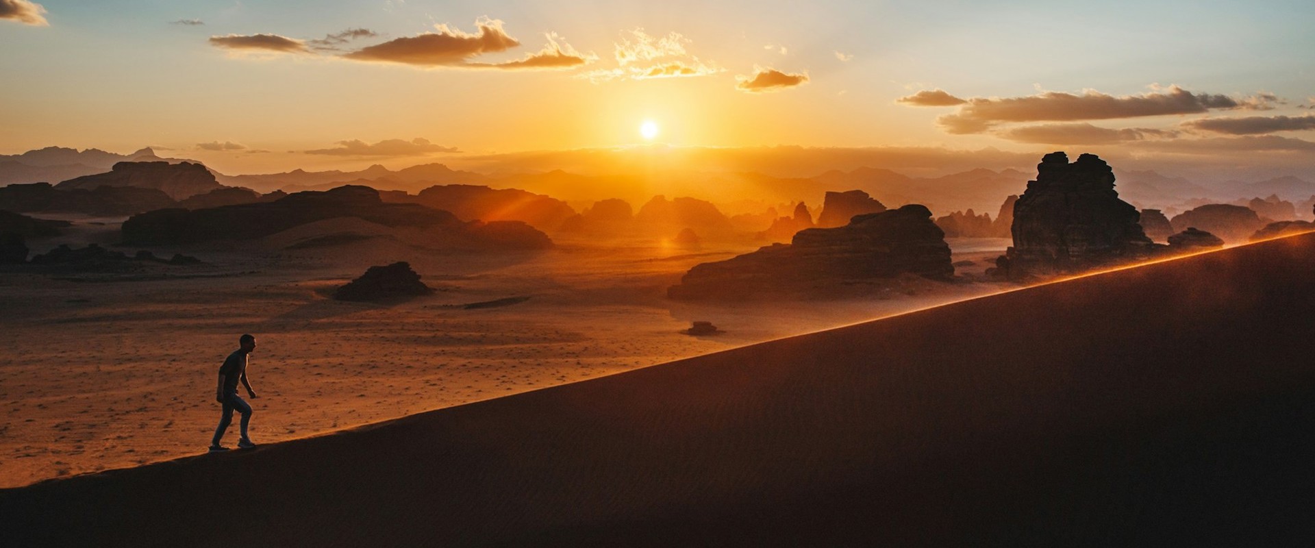 silhouette of man walking up a mountain with sun in background
