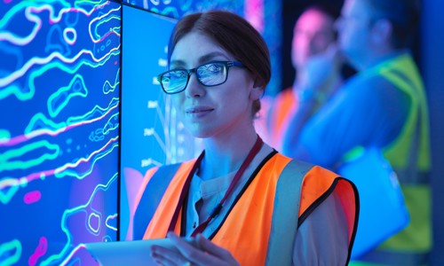A female geologist in a high-vis vest studying a graphical display board holding an electronic tablet