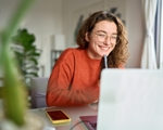 Young woman in glasses smiling at laptop with pen