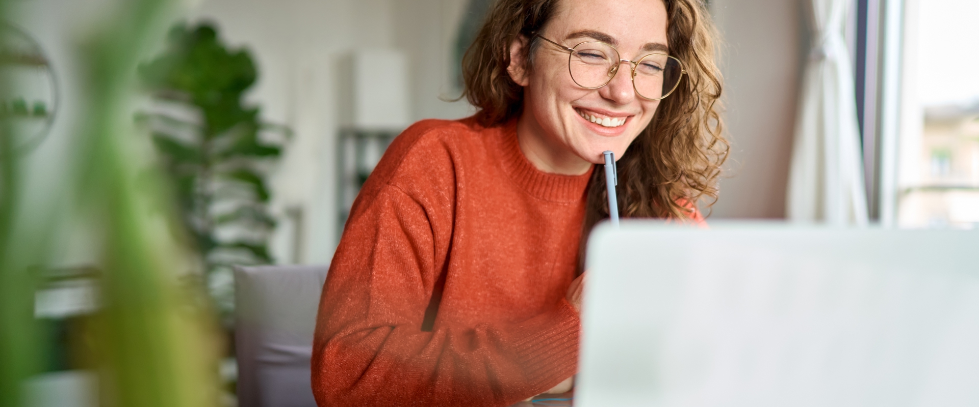 Young woman in glasses smiling at laptop with pen