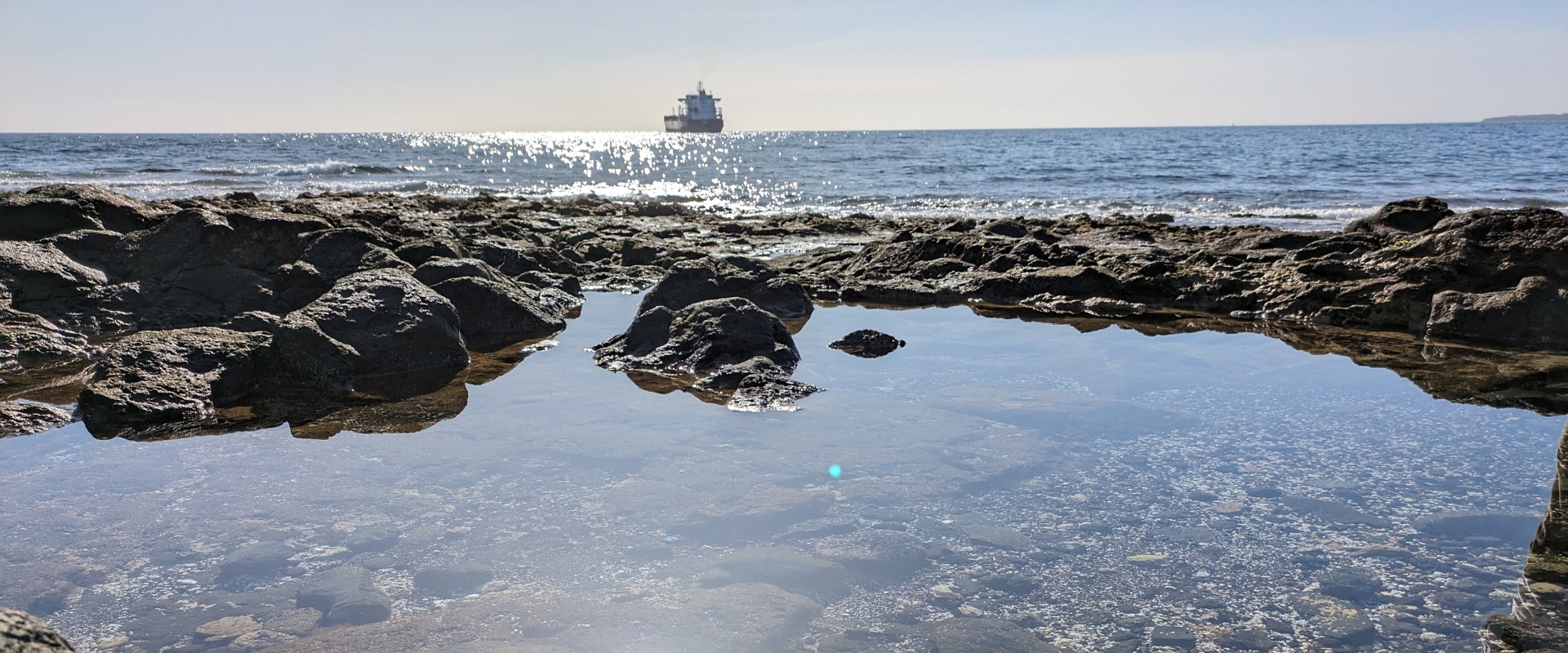 Looking out to the sea from a rocky shore, with a small boat on the horizon