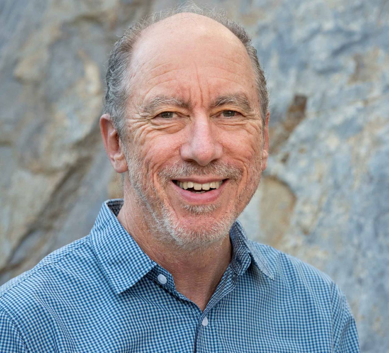 headshot of a white male with short grey hair wearing checked blue and white shirt