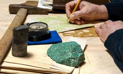 Geologist marking a point on a map accompanied with compass and rock hammer