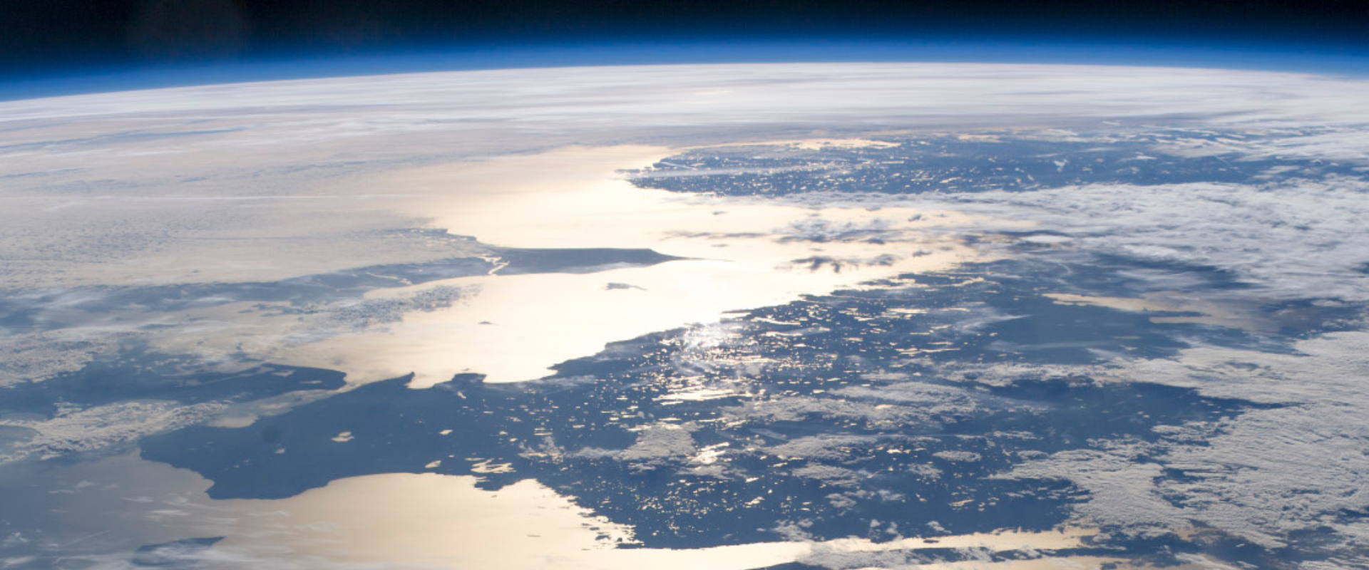 View of Earth from space showing a sunlit coastline, clouds, and the blue curvature of the planet's atmosphere.