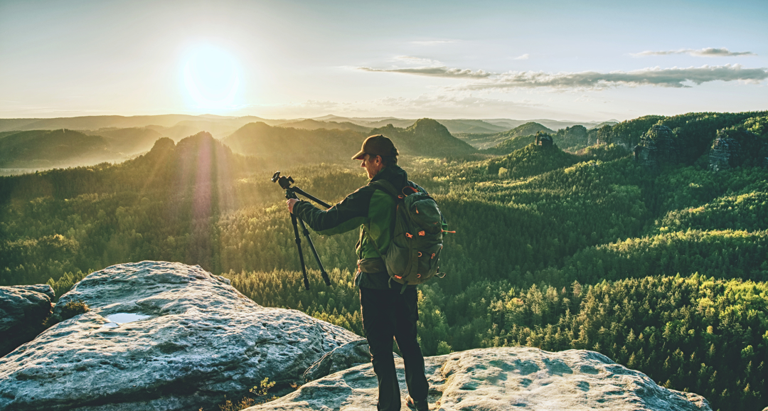 Man on mountaintop holding a camera tripod