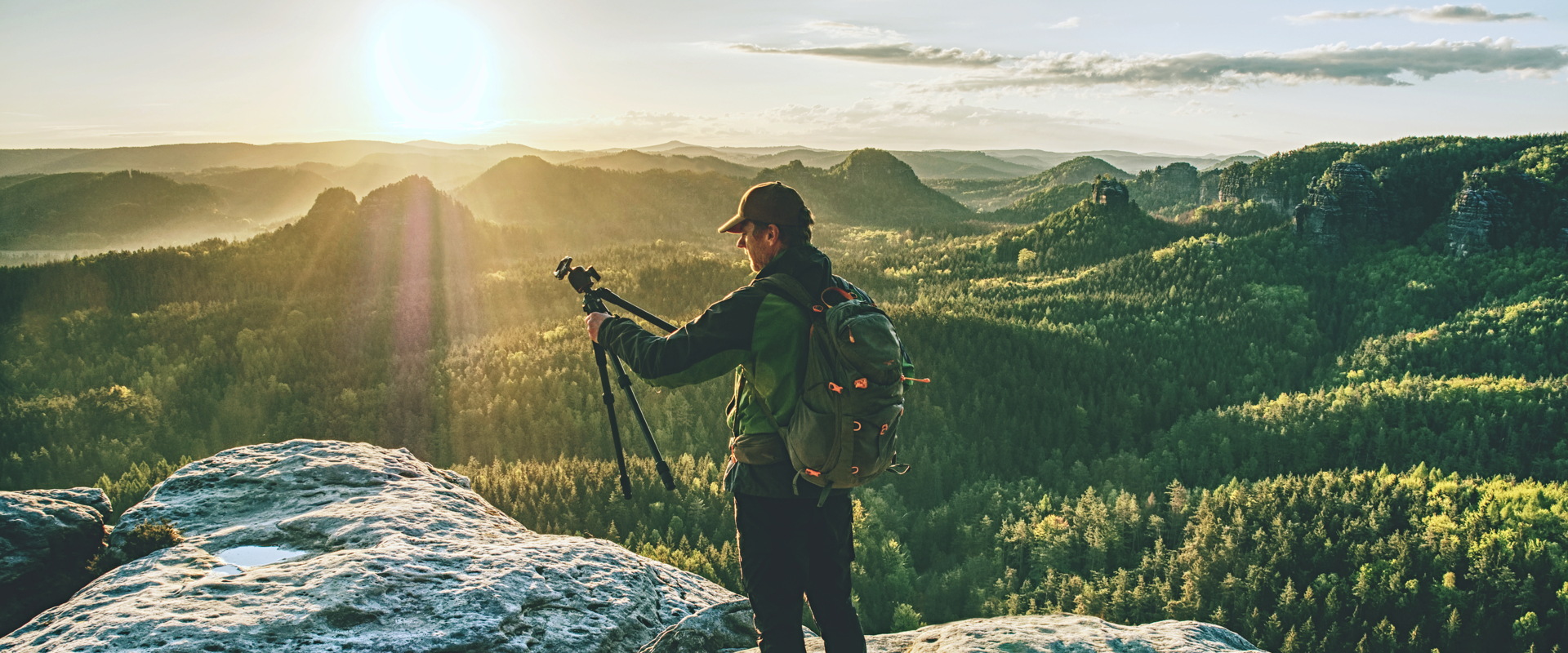 Man on mountaintop holding a camera tripod