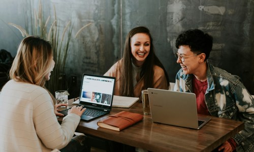 three women working at their laptops together, all smiling