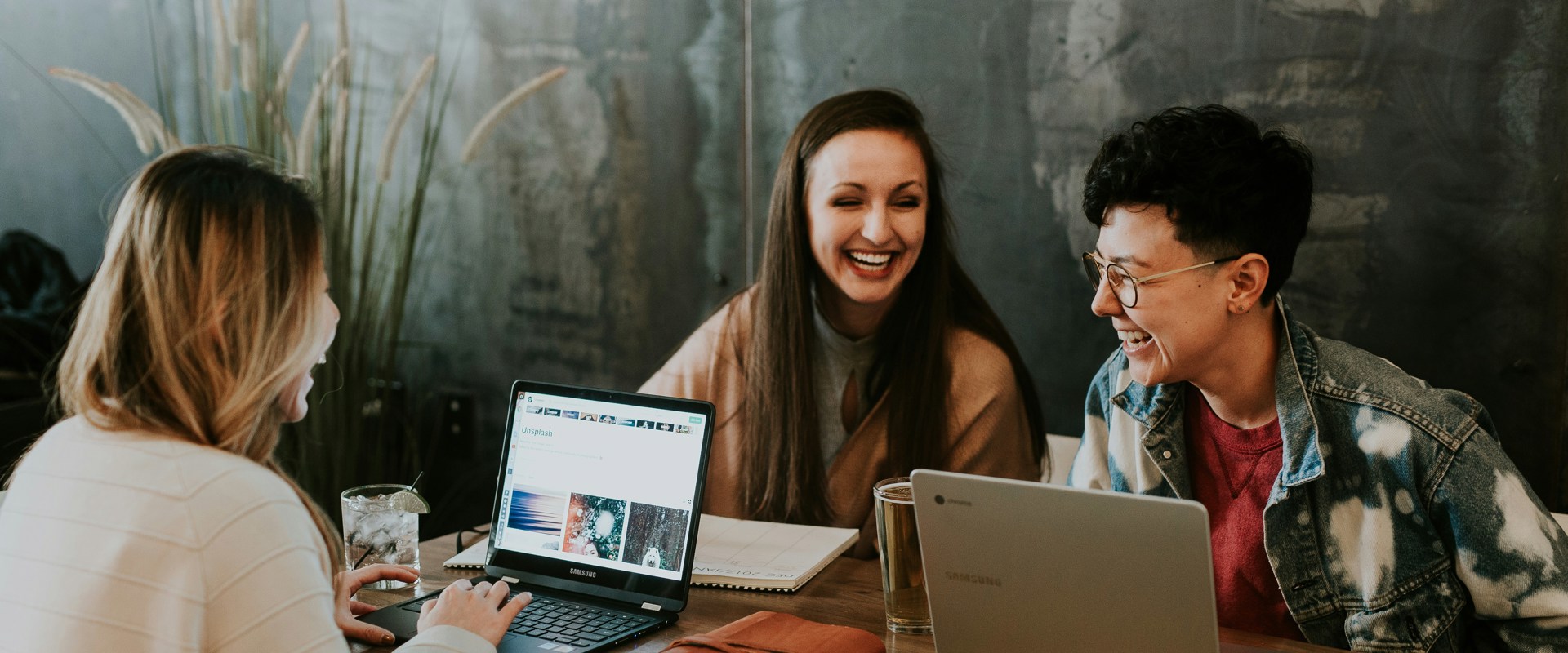 three women working at their laptops together, all smiling