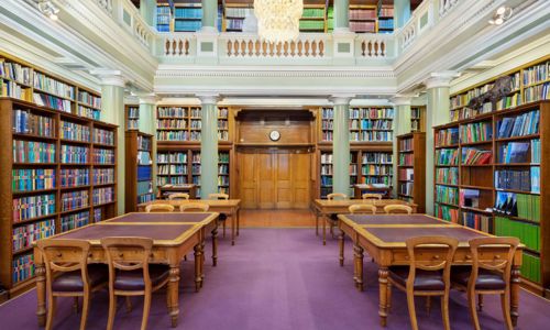 The Upper Library of the Geological Society of London, tables and chairs on a maroon carpet surrounded by book-lined shelves and green pillars