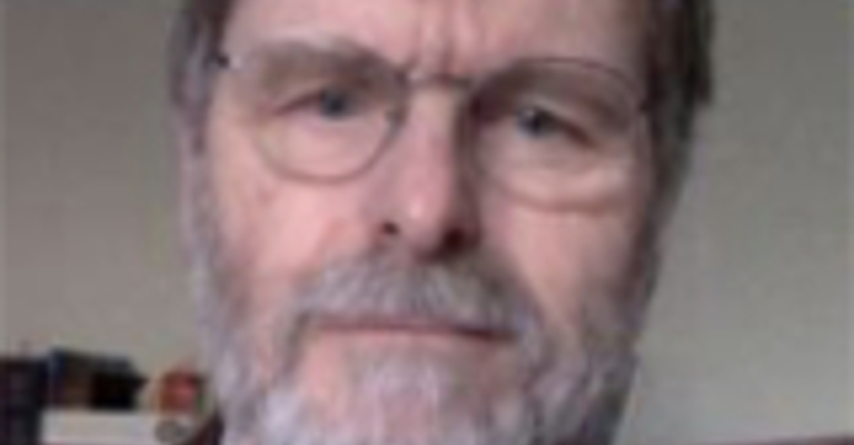 A man with a short grey beard wearing glasses and a dark jacket