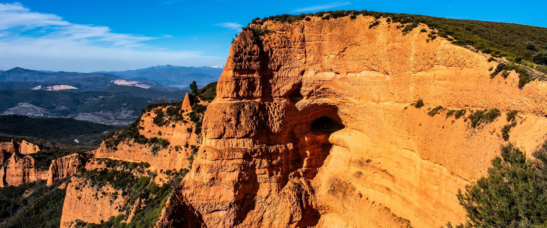 A rocky cliff landscape with blue sky and mountains in the background