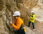 2 people in hardhats with hammers looking at rocks