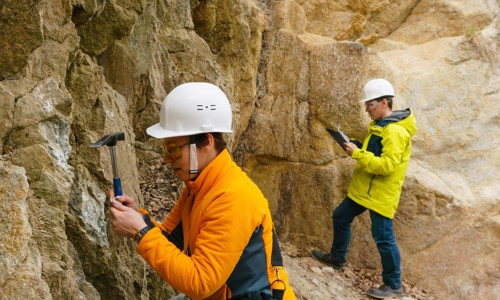 2 people in hardhats with hammers looking at rocks