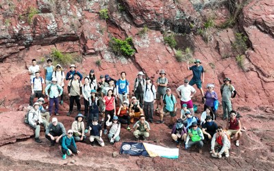A group of people on standing at the bottom of a rocky cliff with a banner on the ground