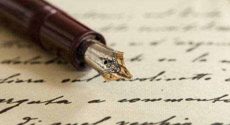 A sheet of paper with black handwriting on which rests the nib and first half of a brown fountain pen